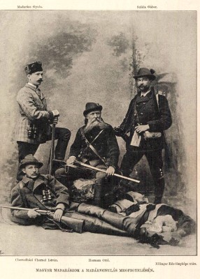 Négy férfi áll és ül egy csoportban, hagyományos magyar vadászruhában, fegyverekkel a kezükben, egy régi fénykép keretein belül.